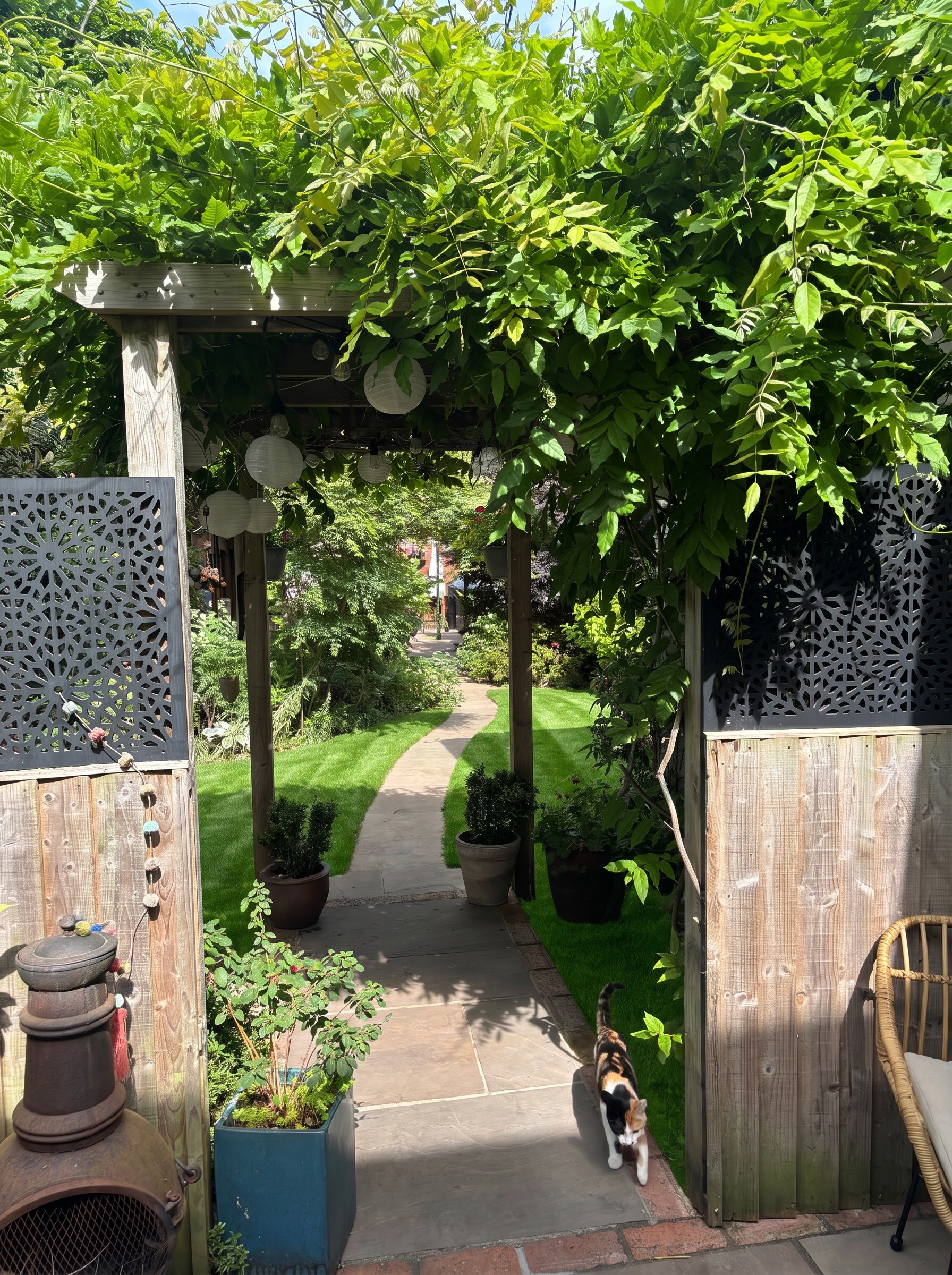 Wisteria-clad pergola arch framing the stone path through the garden