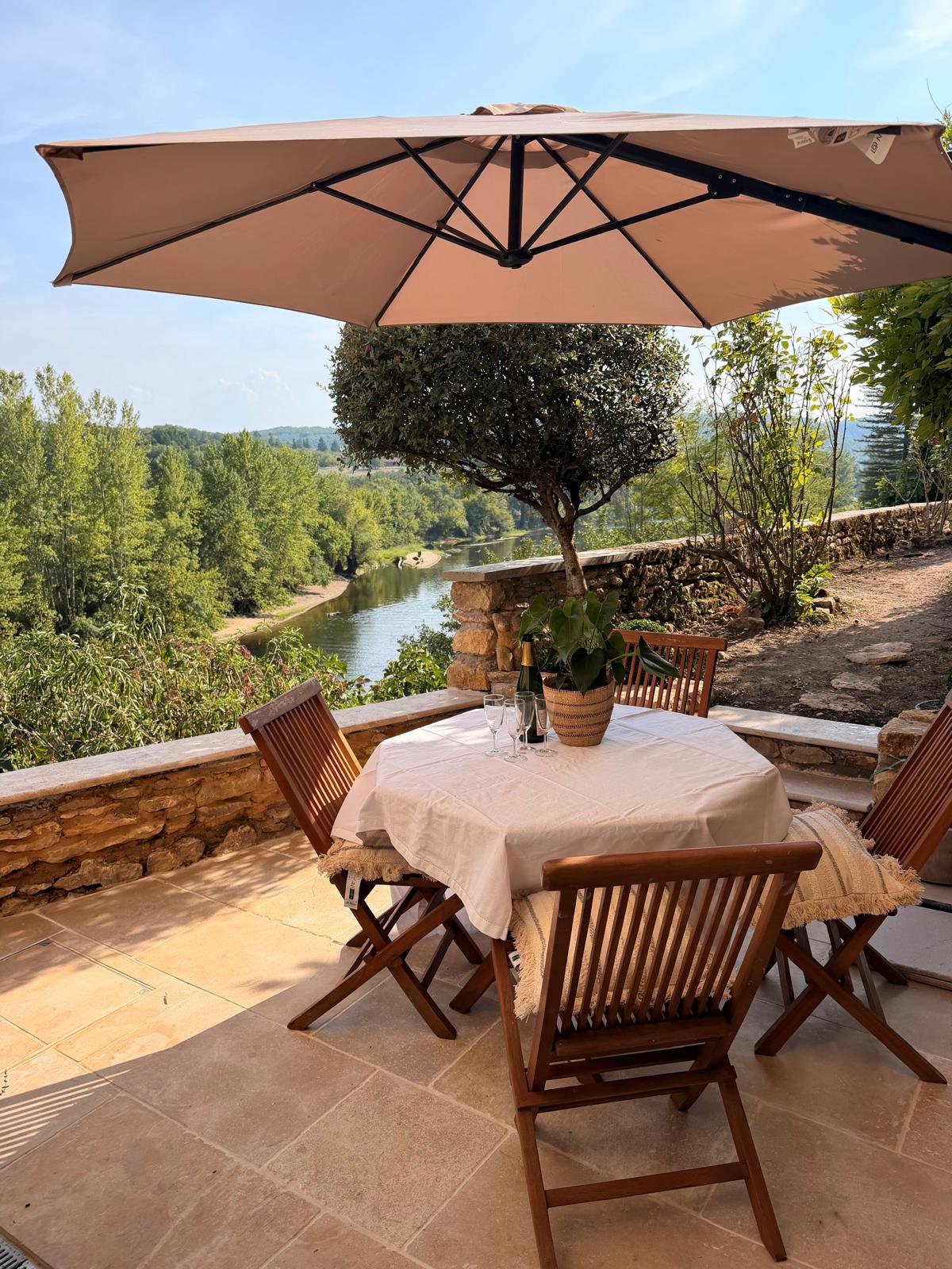 Finished natural stone patio with an outdoor dining set under a parasol overlooking the Dordogne river