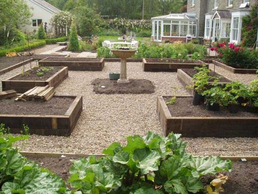 Formal kitchen garden with sleeper-edged raised beds and central stone fountain designed by Sil Landscapes