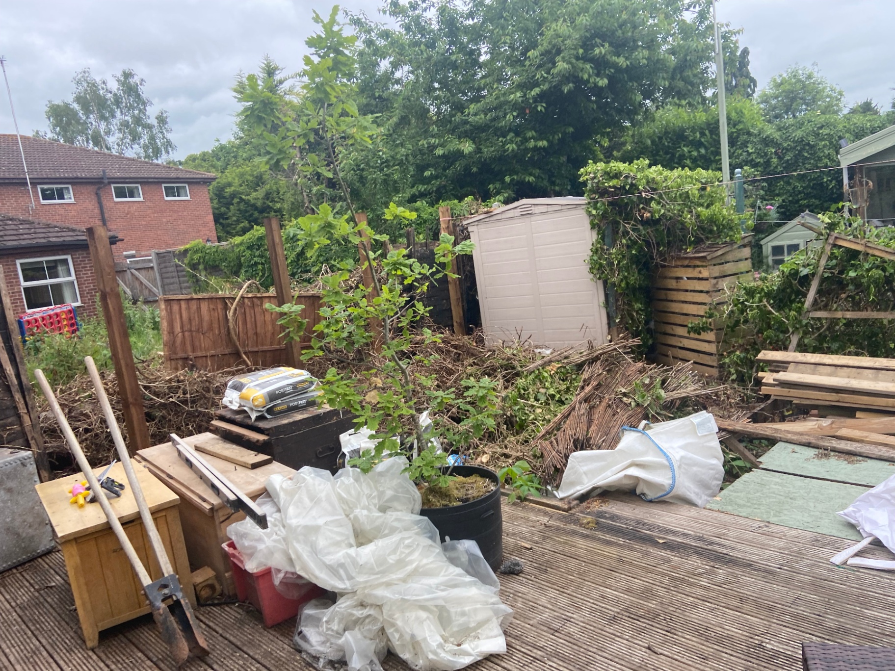 Overgrown courtyard piled with debris and rotten decking before clearance