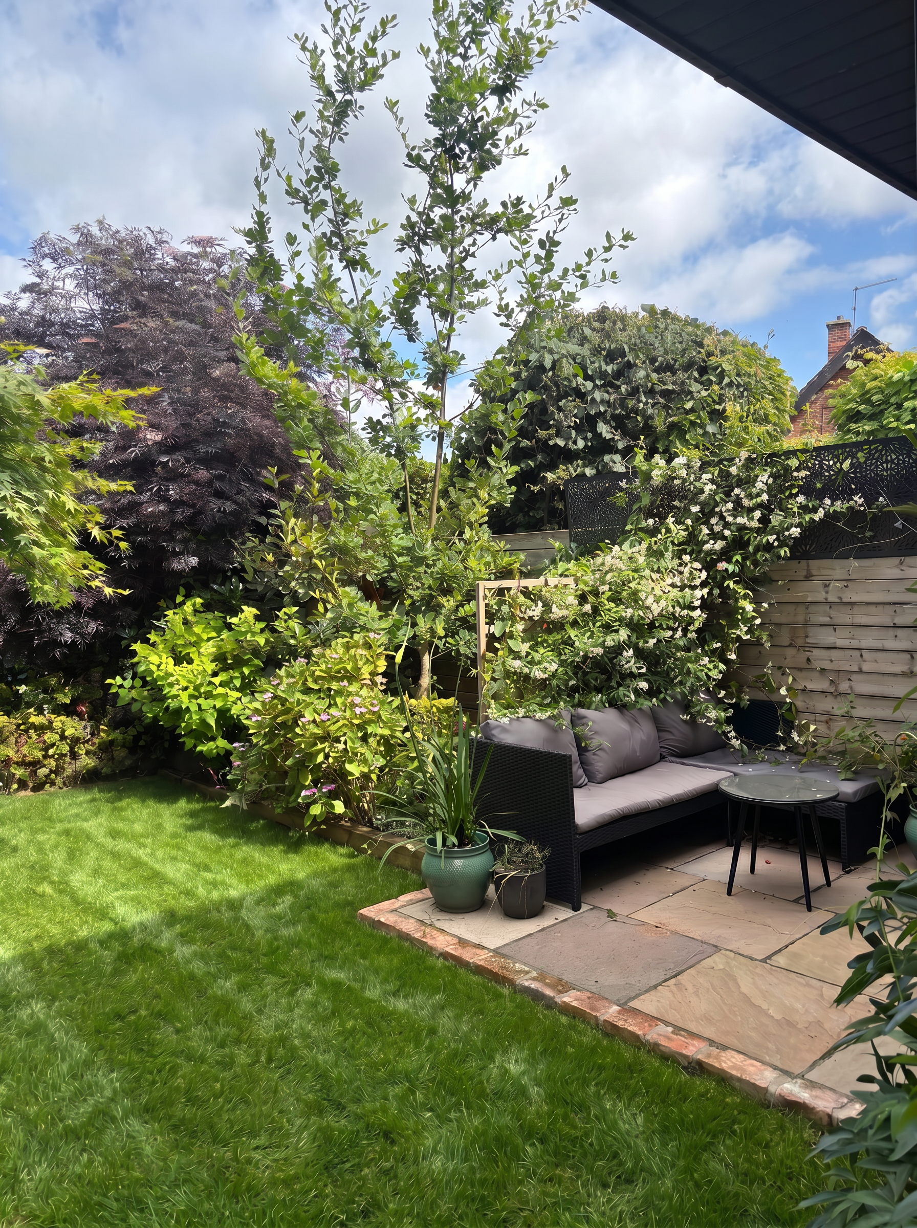 New patio with sofa, jasmine-covered trellis and mature planting